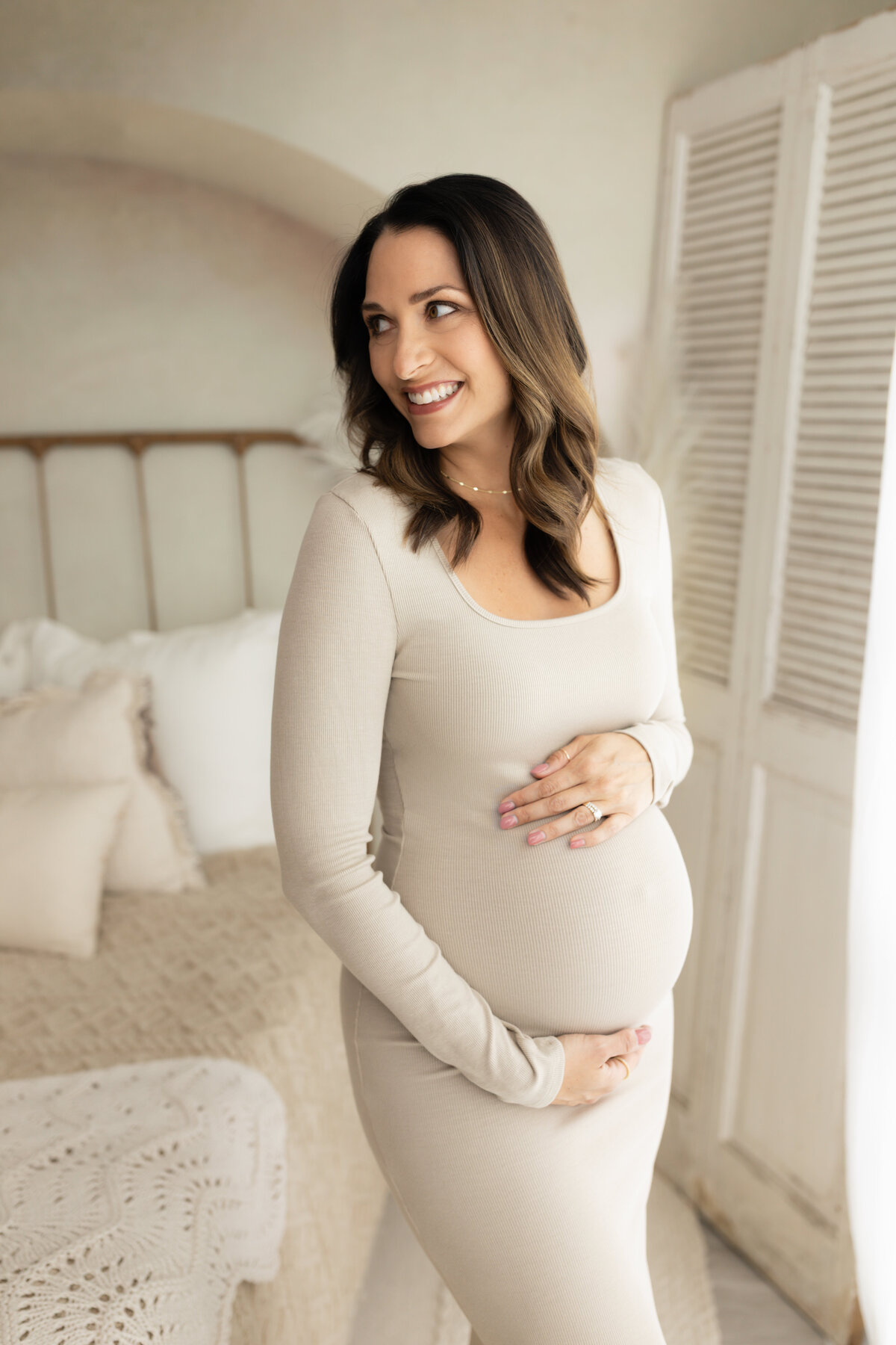 pregnant mother in beige maternity dress holding baby bump for maternity photoshoot