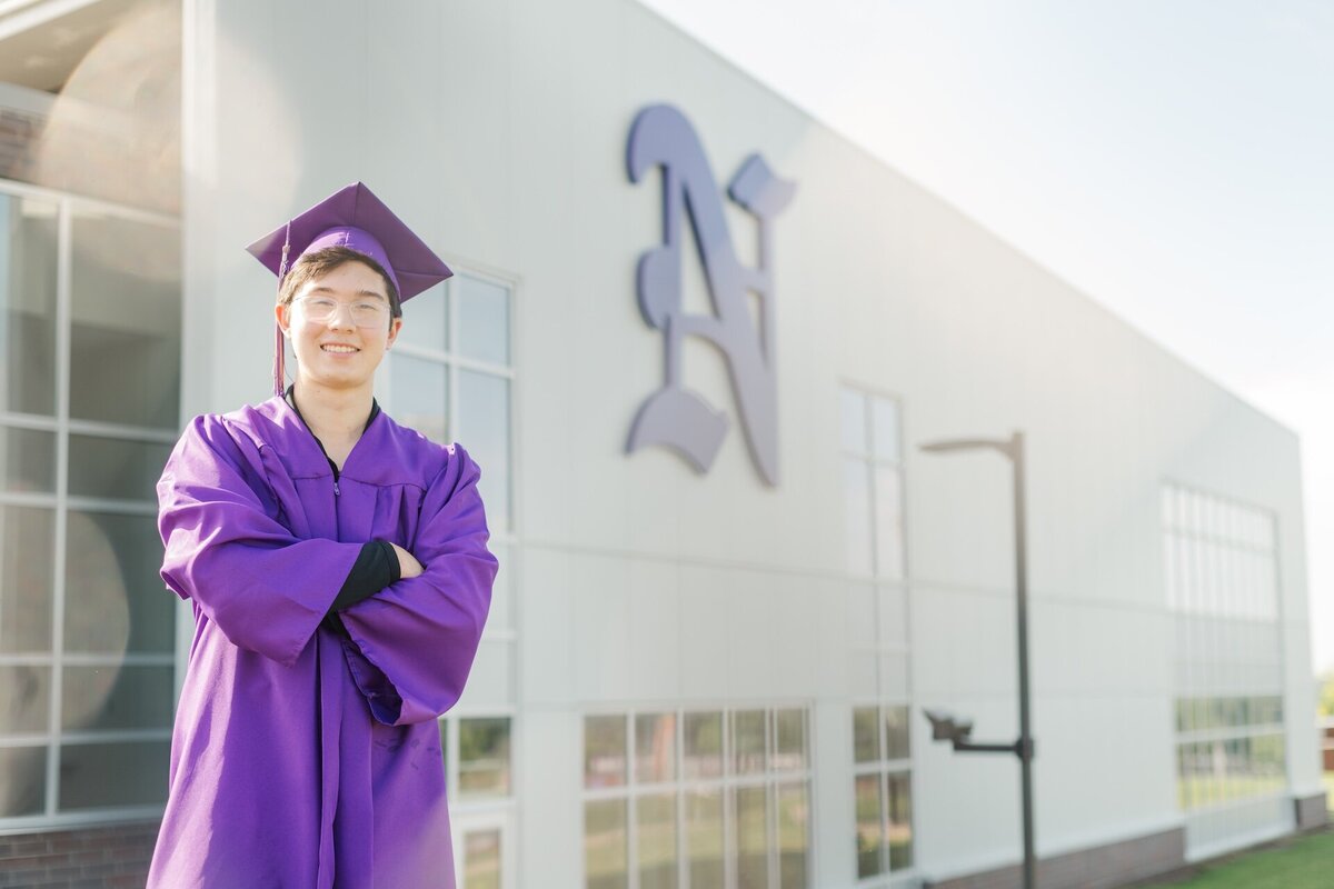 a guy in a purple cap and gown standing in front of his school