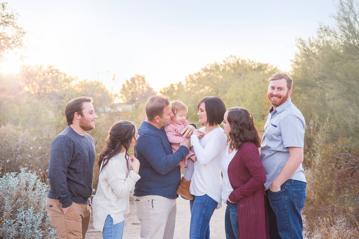 Family in white, blue, and maroon on a desert path playing with redheaded toddler