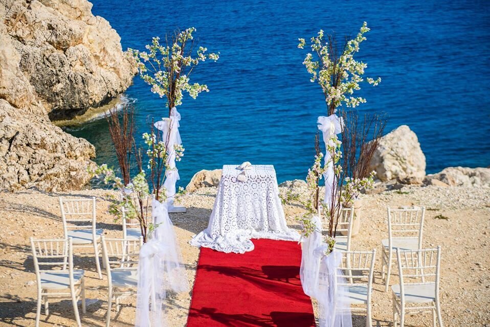 A red carpet aisle leads to a table decorated in white lace at the edge of seafront clifftop