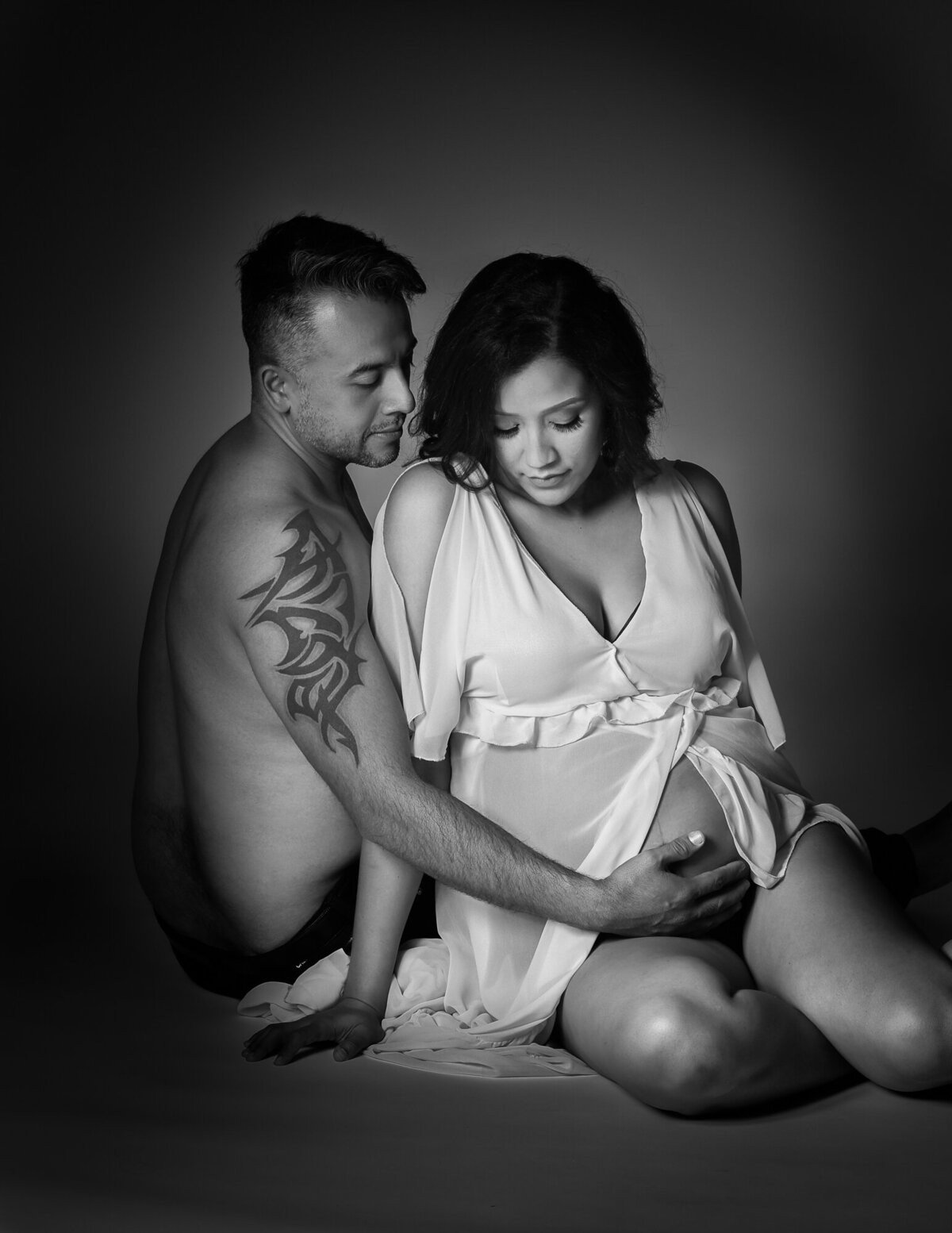 Black and white portrait of husband and pregnant wife lovingly looking down at the baby bump