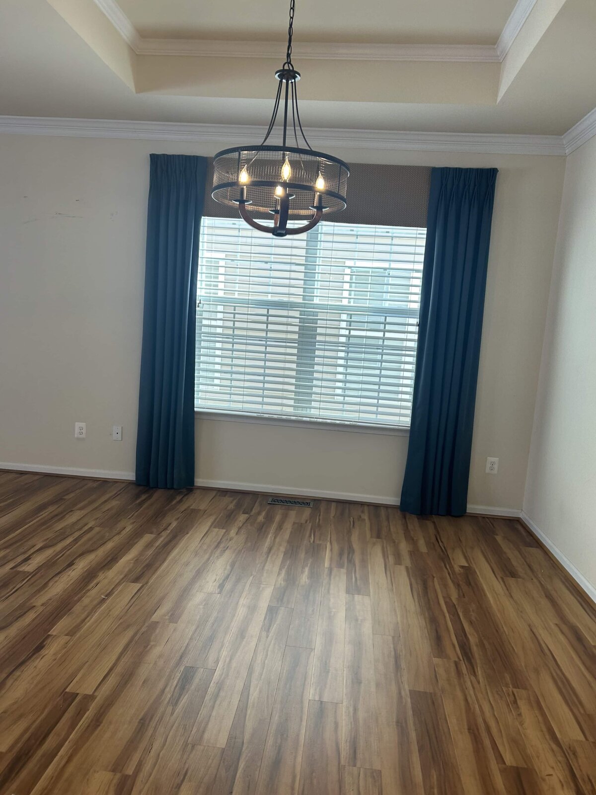 Empty room with hardwood floors, chandelier, and large window with navy curtains — Williamsburg home before staging.