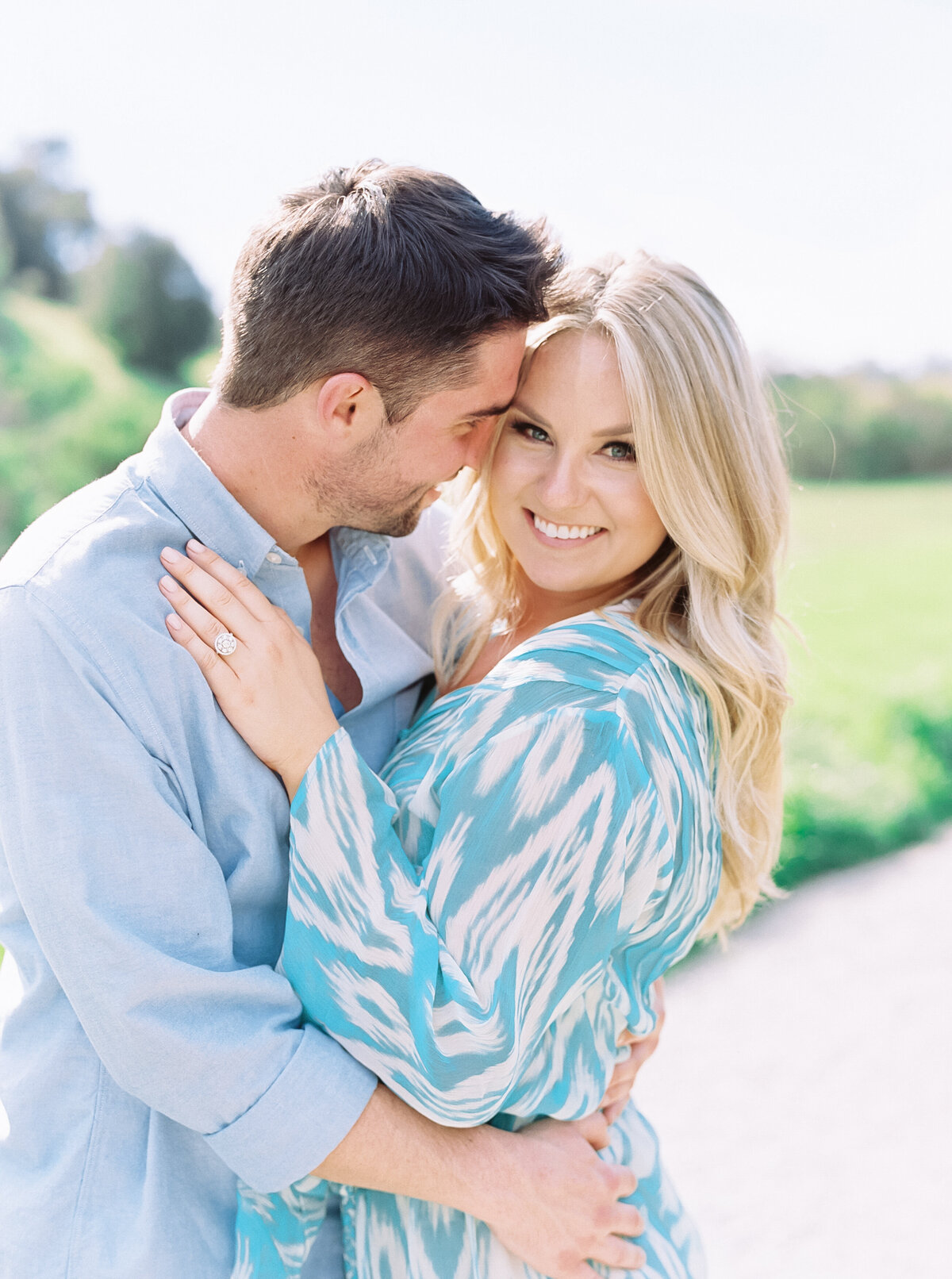 Man in blue shirt kisses his beautiful fiancee while she looks at the camera.