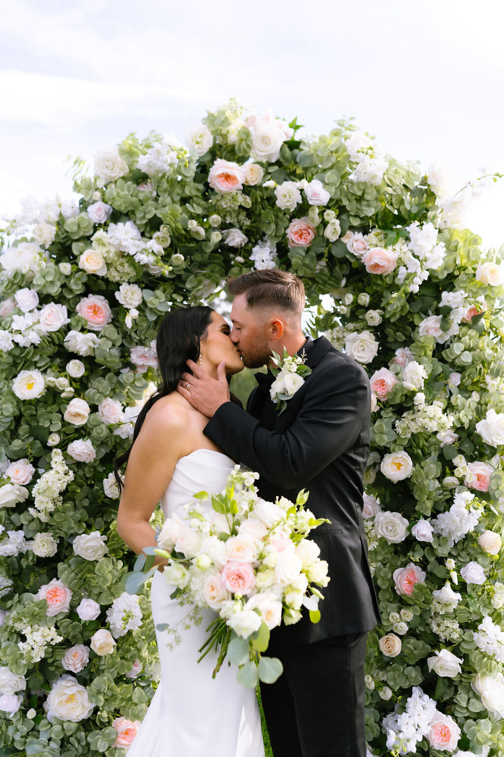 Couple kissing in front of a floral arch