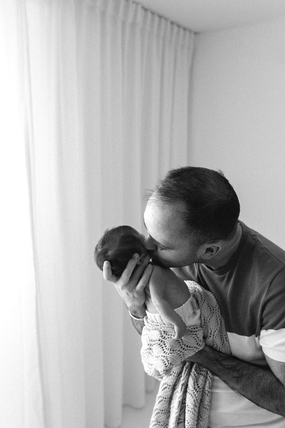 Dad kisses baby on cheek in black and white photo