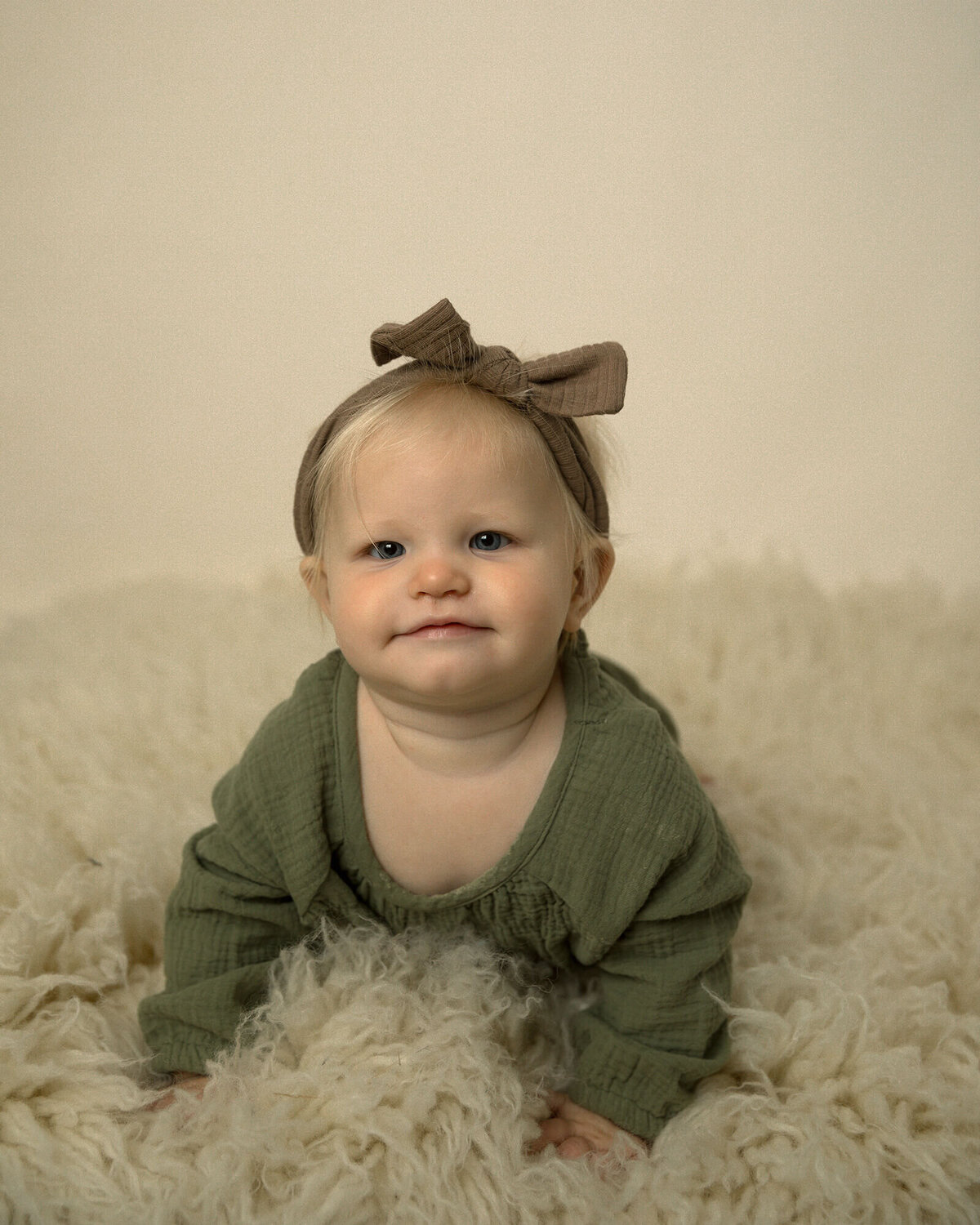1 year old girl with green shirt on her belly on creme colored rug.