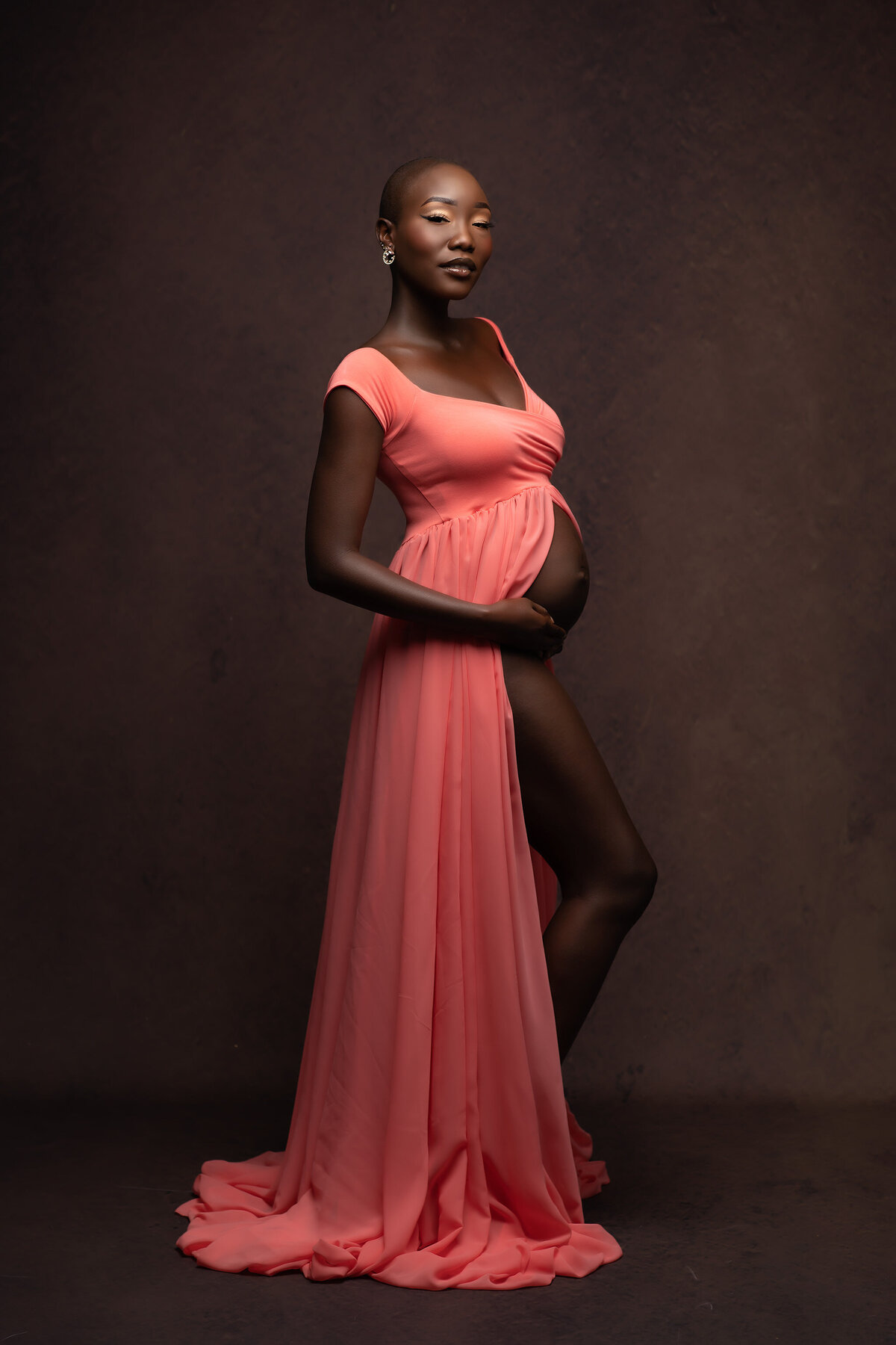 A graceful photograph showcasing an expecting mother wearing a flowing coral dress, captured against a rich textured backdrop. This stunning portrait exemplifies elegant Dallas maternity photography.