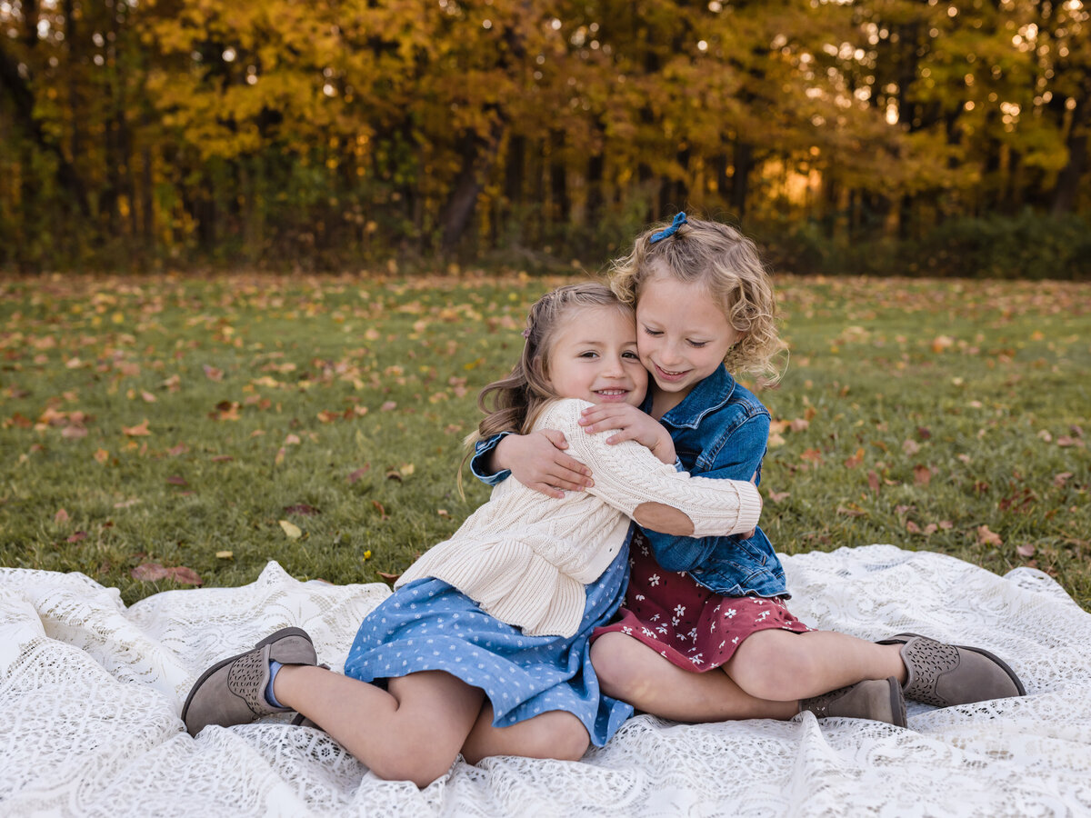 sisters sitting on lace blanket hugging for family photos