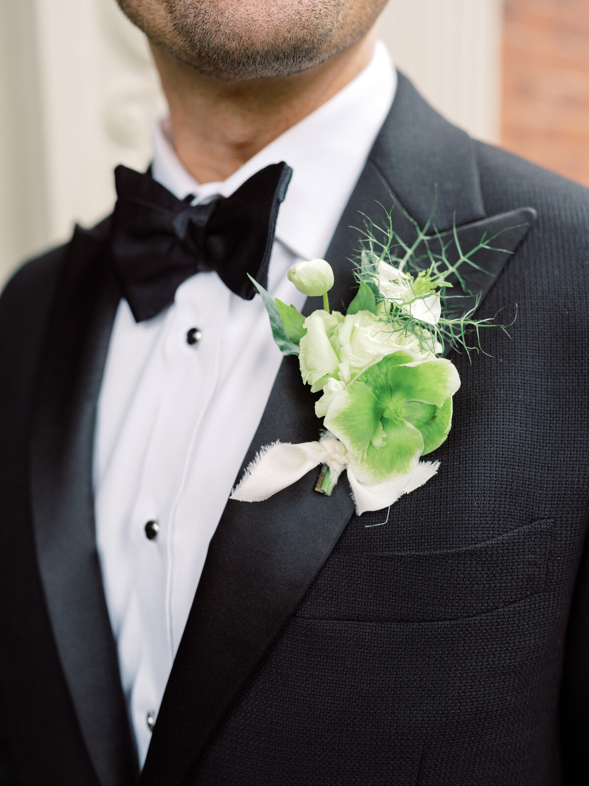 An artistic close-up of the groom's floral boutonnière, featuring vibrant greenery and delicate flowers, symbolizing love, style, and attention to detail in wedding aesthetics.