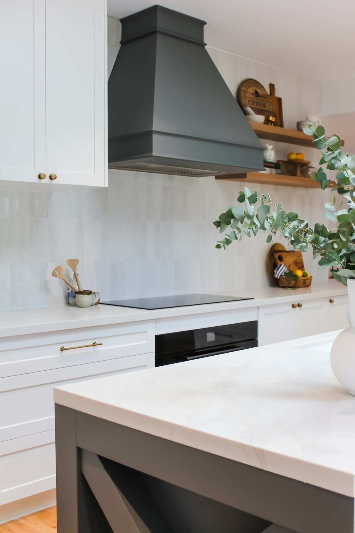 Modern kitchen in Newcastle with white cabinets, marble countertops, and a dark range hood. Eucalyptus plant on the island, reflecting the luxury home design style expertly curated by renowned Newcastle interior designers.