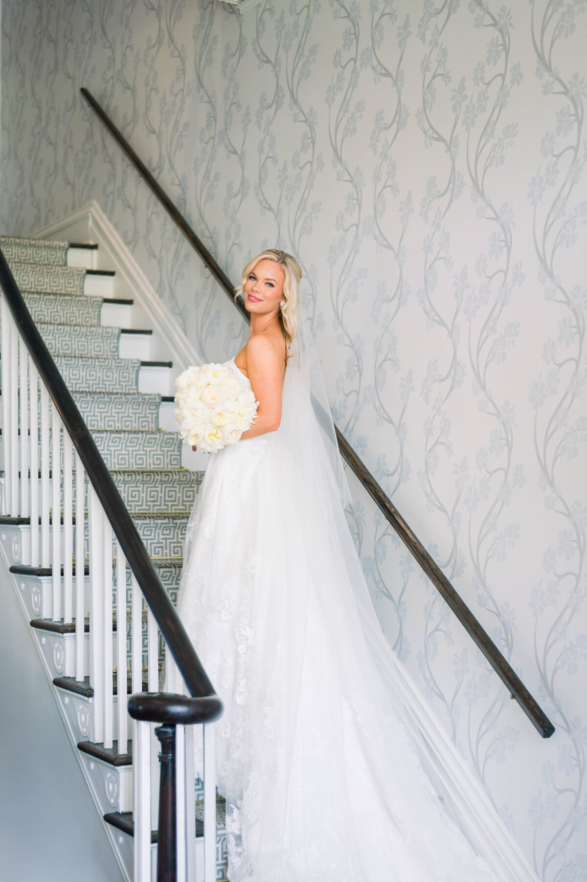 Bride in a Robert Bullock wedding dress standing on the stairs of the University Club in Tuscaloosa, Alabama during a romantic summer wedding

