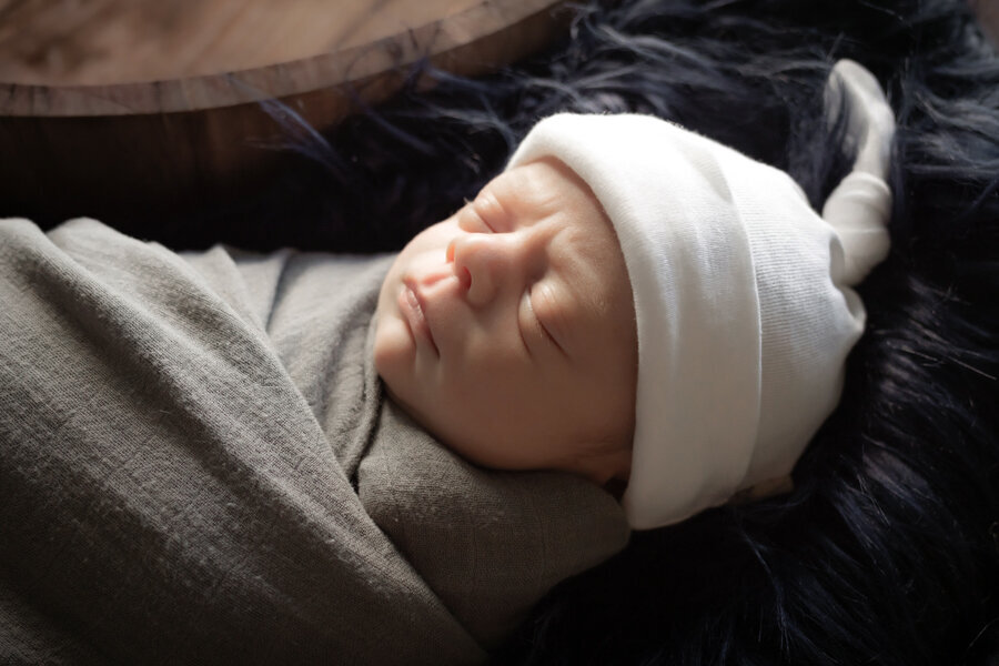 Newborn baby with with white had and grey swaddle.