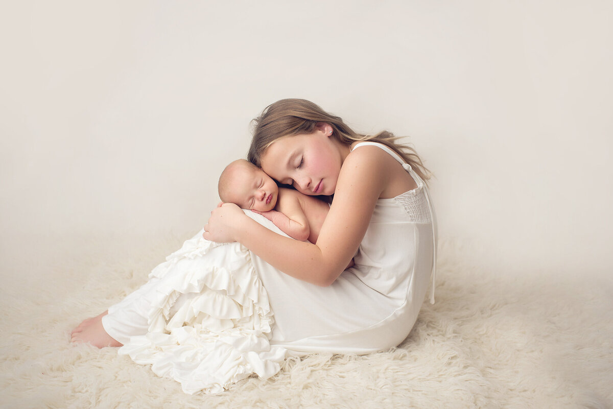 sisters posed together with the younger baby girl in the older sisters arms