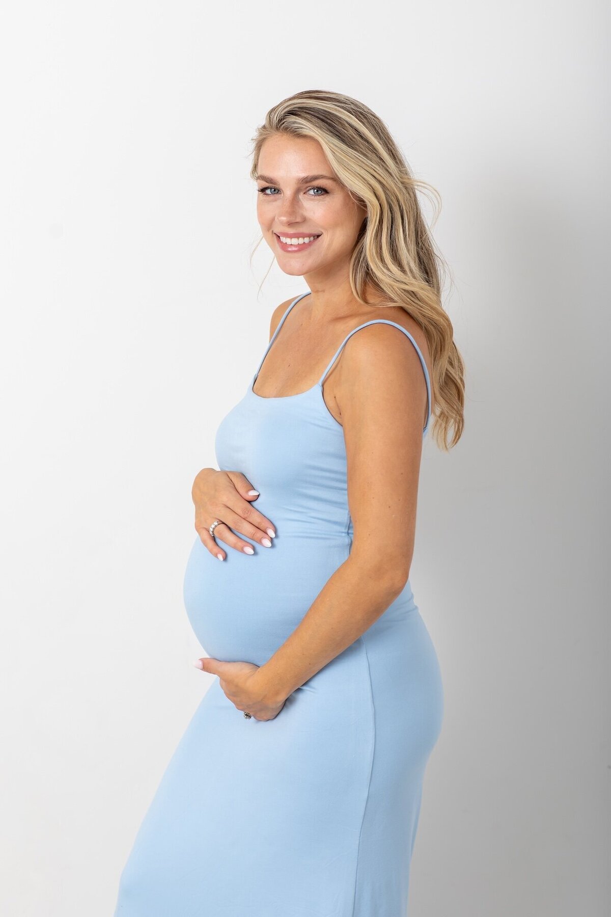 Elegant maternity portrait of a woman wearing a form-fitting blue dress