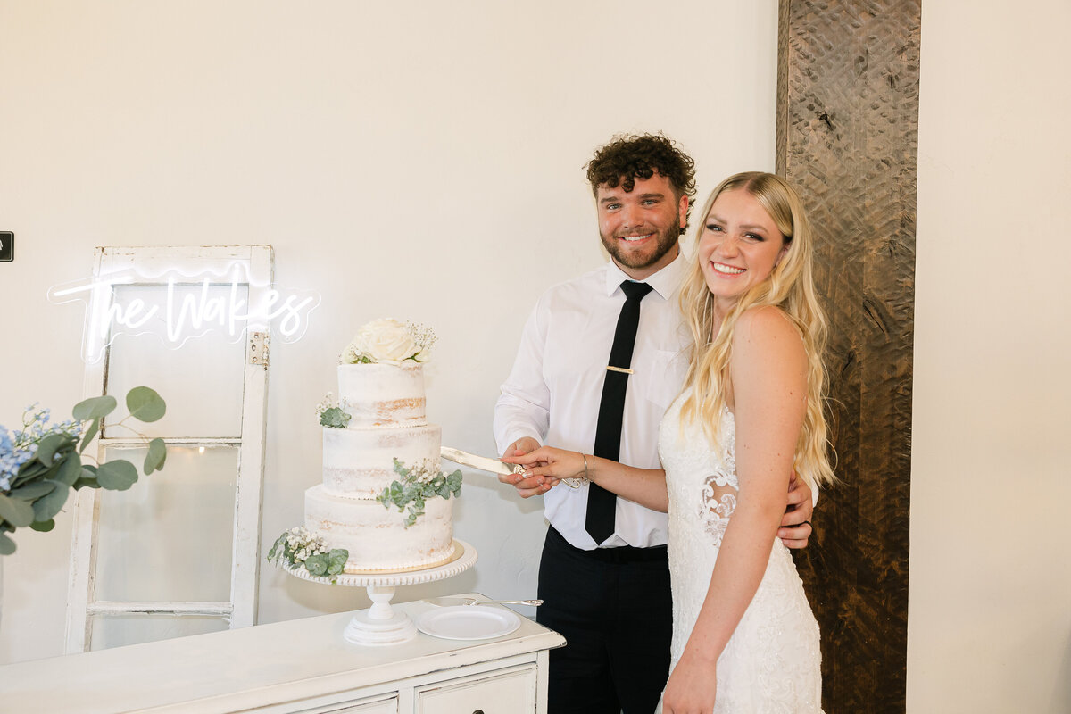 Couple cutting their cake in front of a neon sign