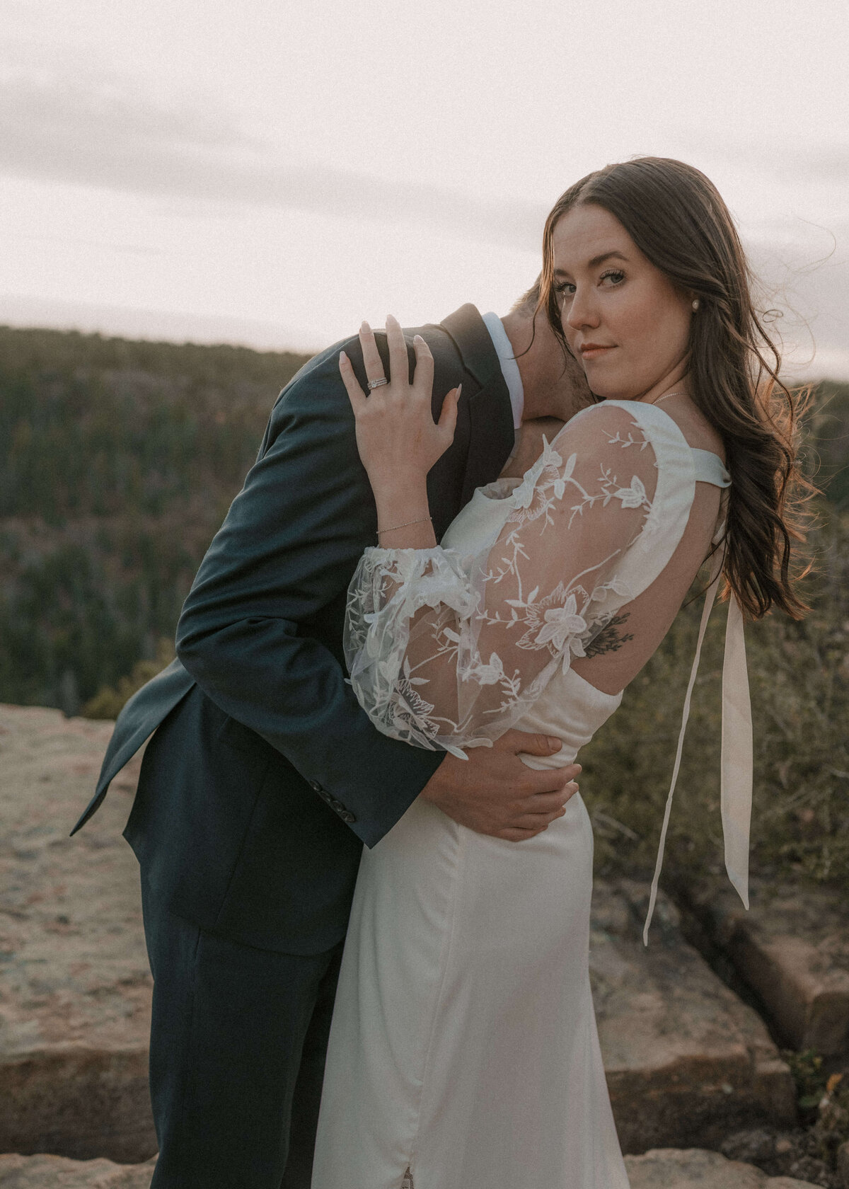 groom leaning in and embracing bride while she looks at camera during elopement on Mogollon Rim on Payson, Arizona