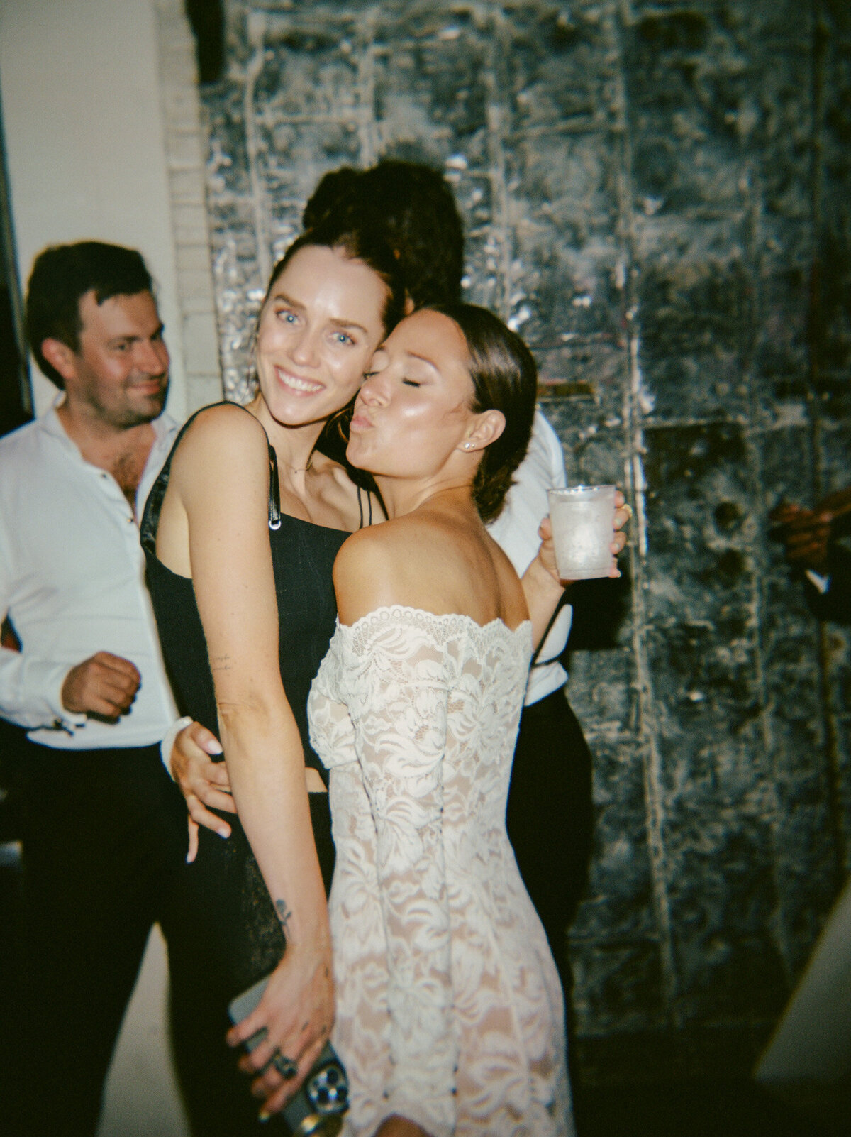a bride in a fitted lace second dress poses with her friend for a natural film photo