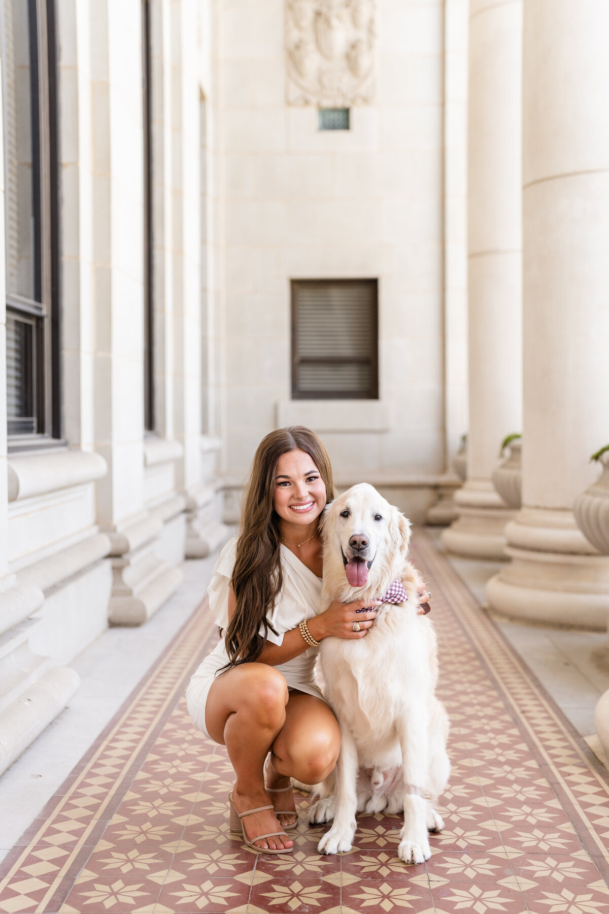 Texas A&M senior girl hugging dog and smiling while wearing white dress in the columns of the Administration Building
