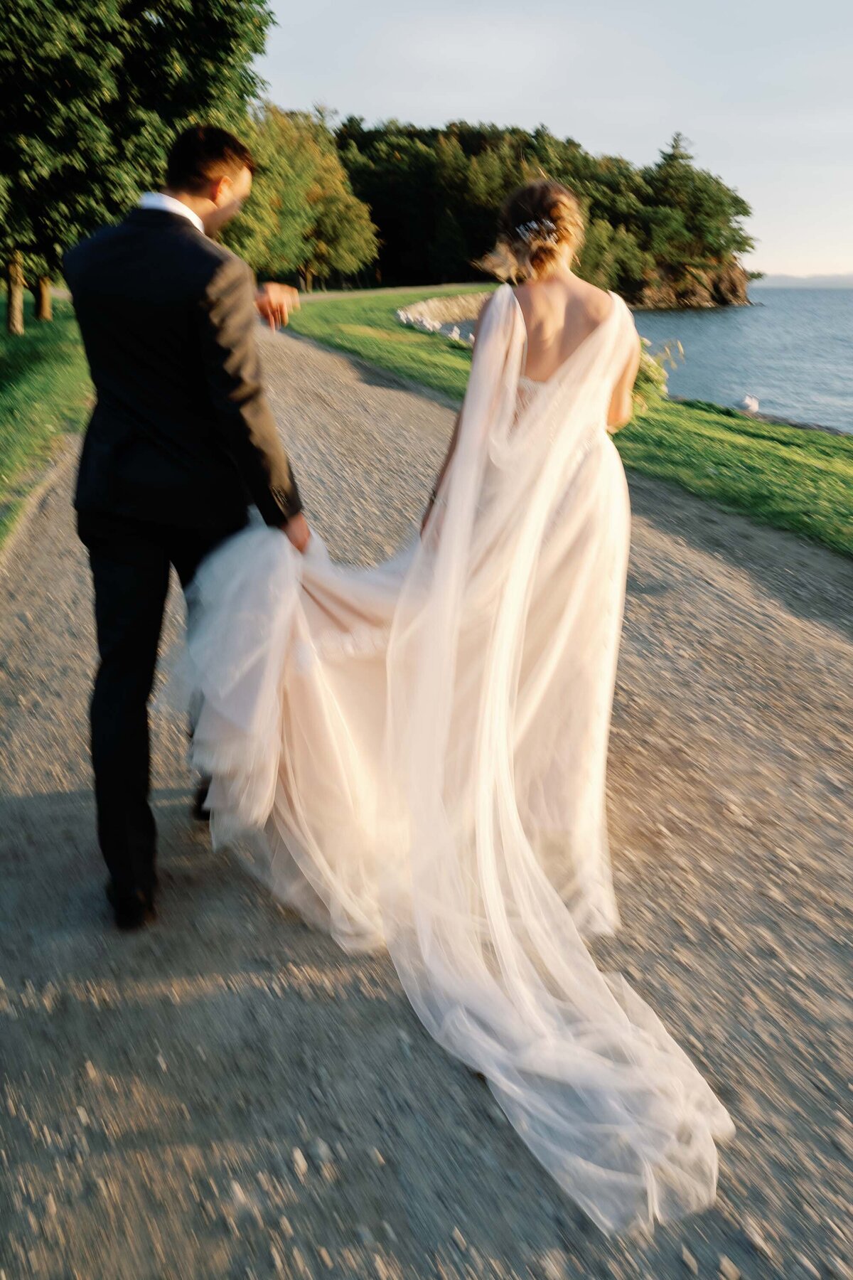 bride and groom walk down stone path with train catching the wind in vermont