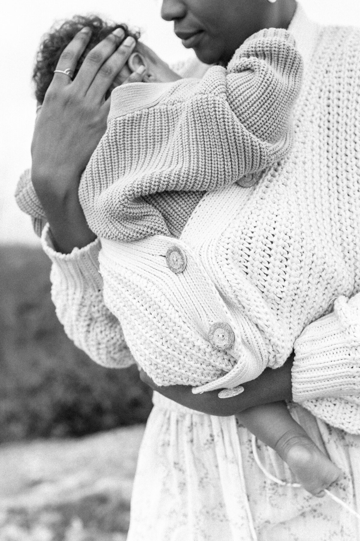 A black and white portrait of a mother snuggling her baby in her sweater during his newborn session at a Kansas City park. 