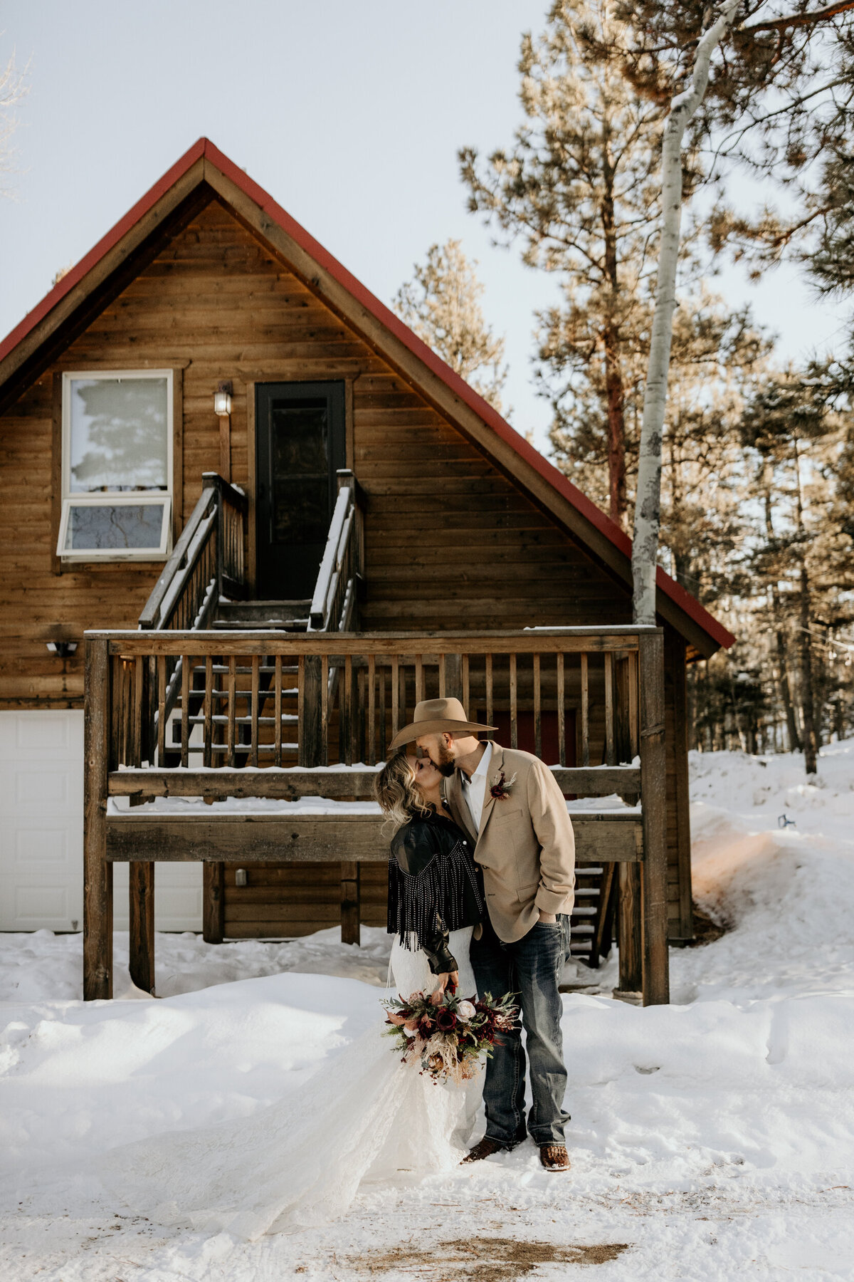 bride and groom kissing in the snow in front of an Angel Fire, NM cabin