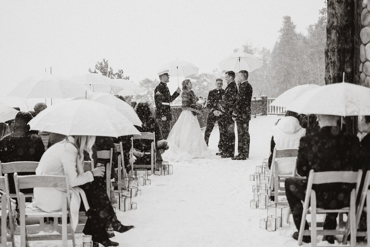 Snowy outdoor wedding at The Lodge at Breckenridge with guests holding umbrellas during the ceremony.