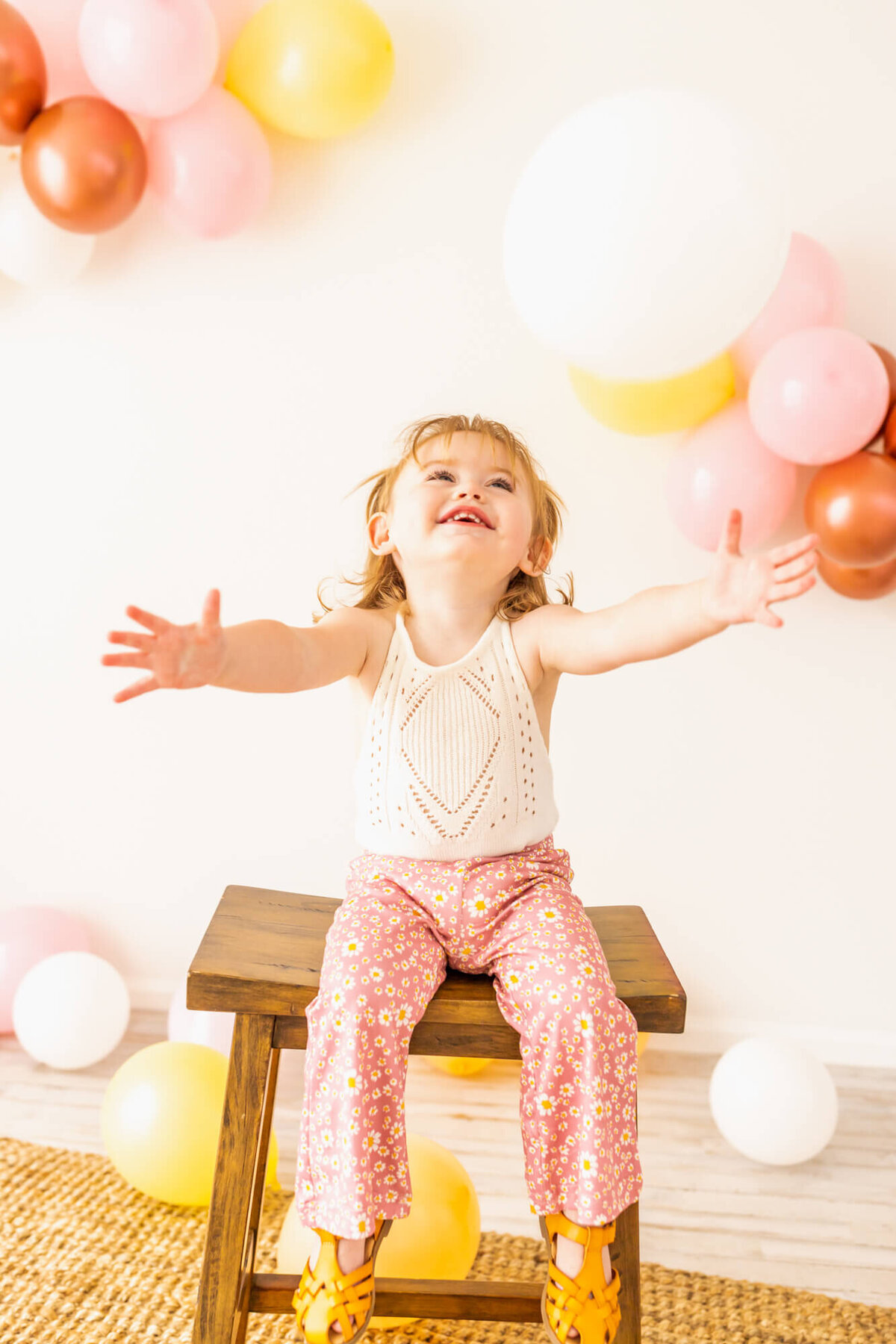 Toddler girl dresses in bell bottoms and a lace romper sitting  and trying to catch colorful balloons