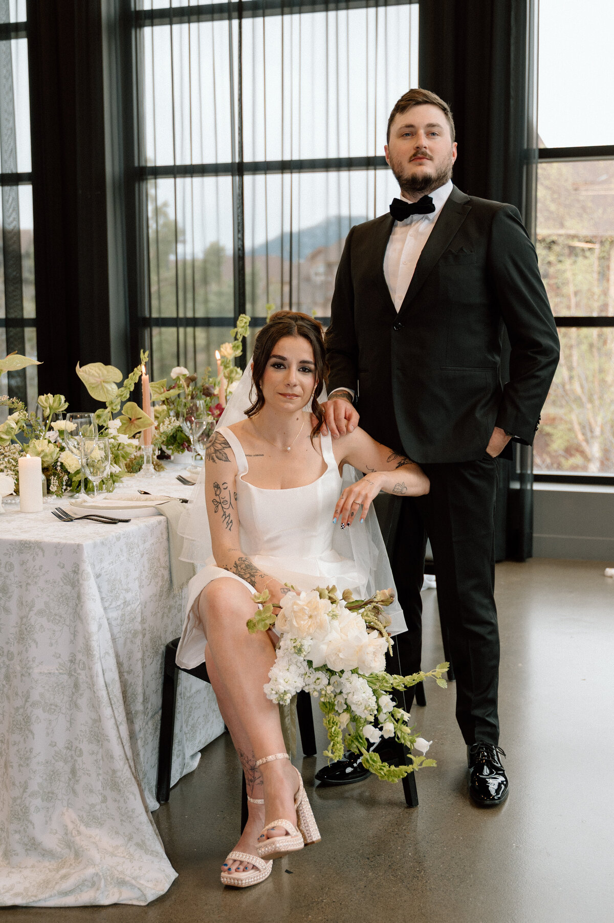 Groom in black tuxedo standing behind his bride during elegant indoor wedding session.