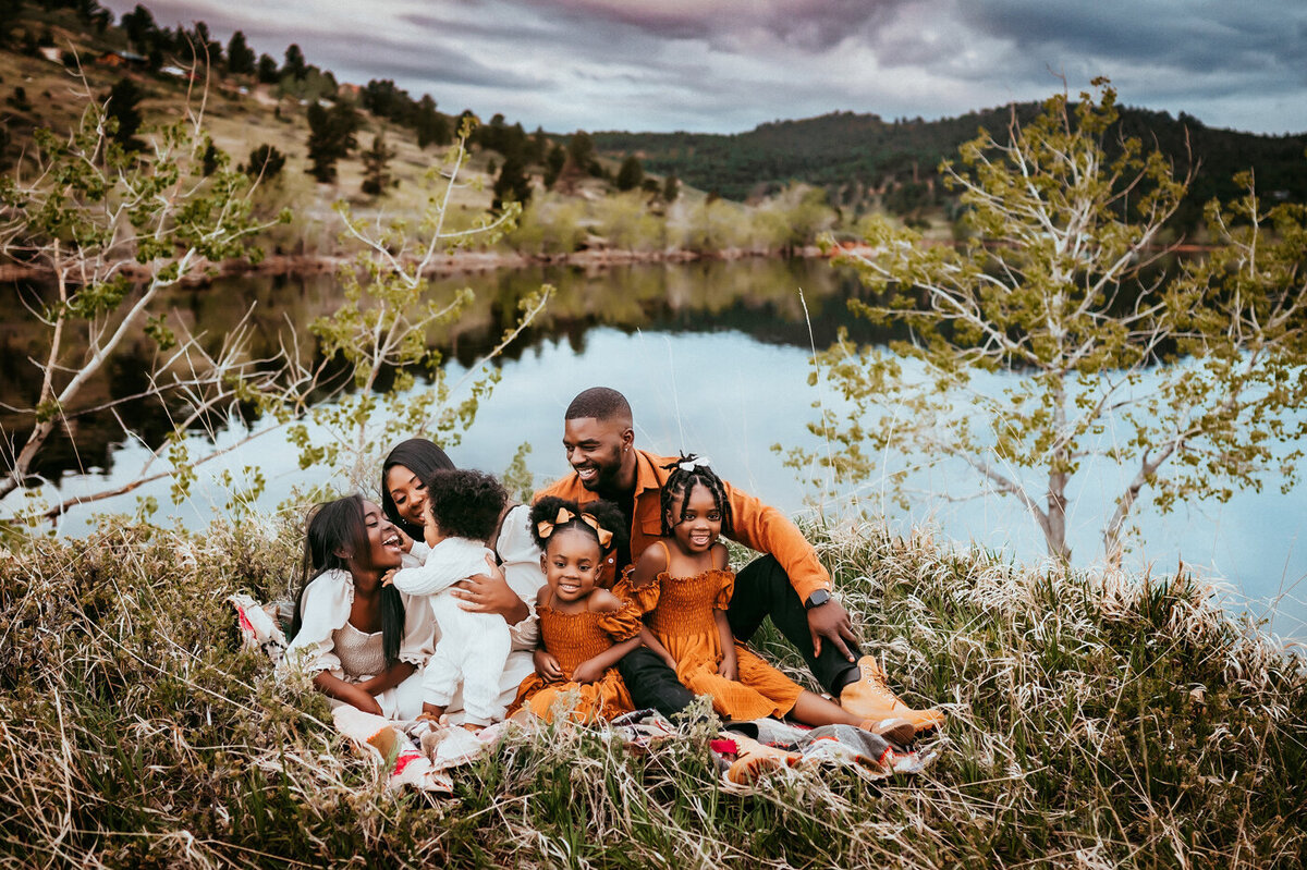 Family snuggling on blanket in front of a beautiful lake backdrop