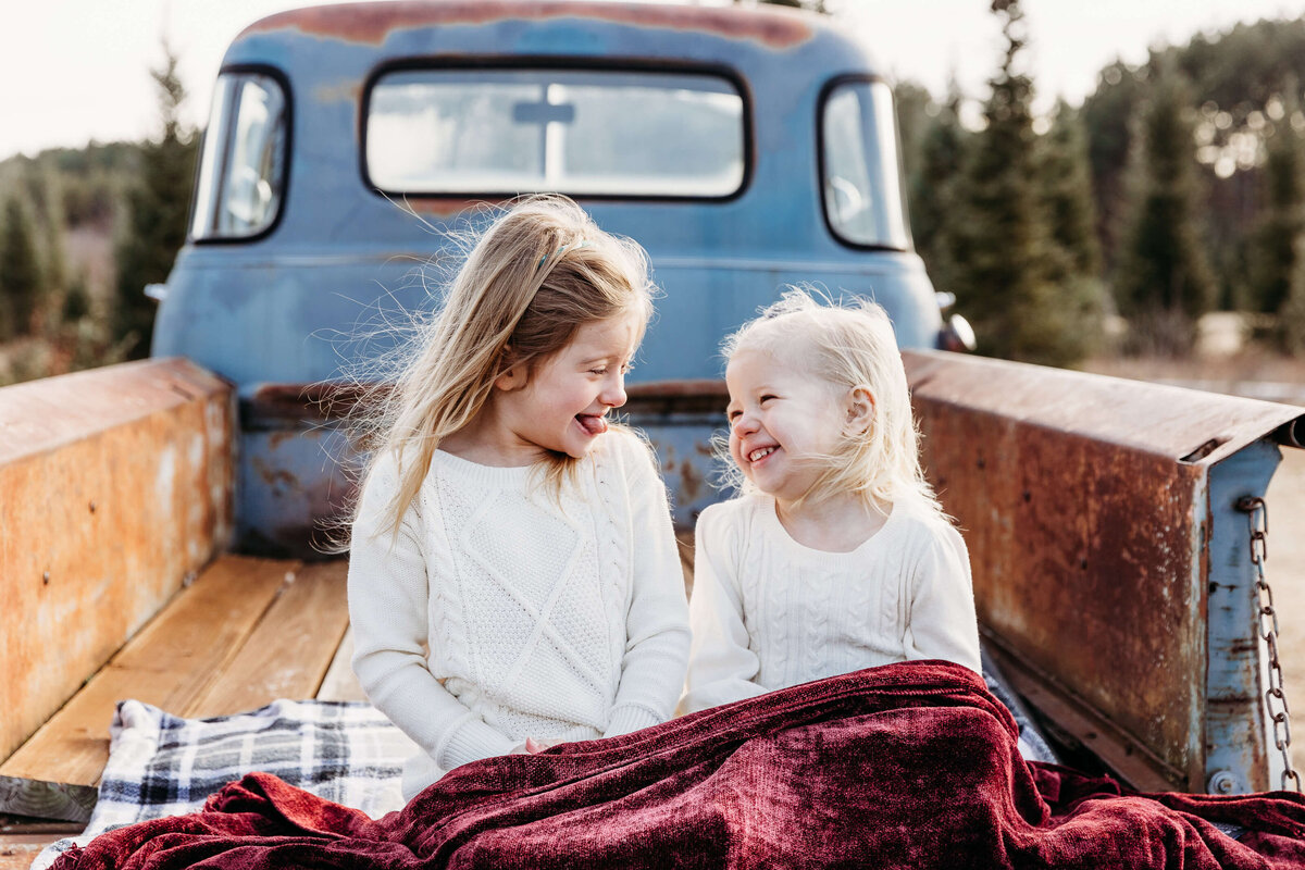 sisters making silly faces in the back of an old truck for family photos