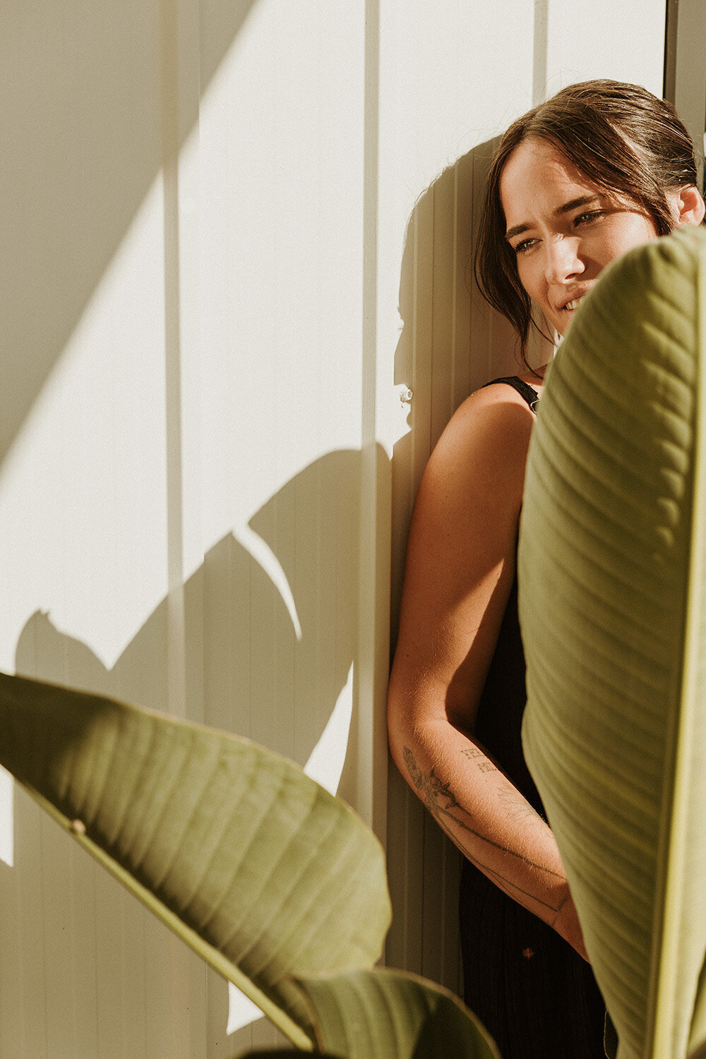 Woman leaning into the sun, smiling behind a palm leaf — a warm, joyful brand photo by Sunshine Coast branding photographer.
