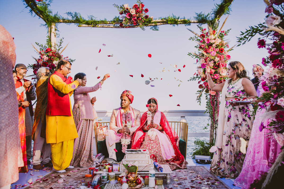 Roses being thrown over the fusion indian black bride and groom during their hindu ceremony at sunset at chateau la mer in long island ny