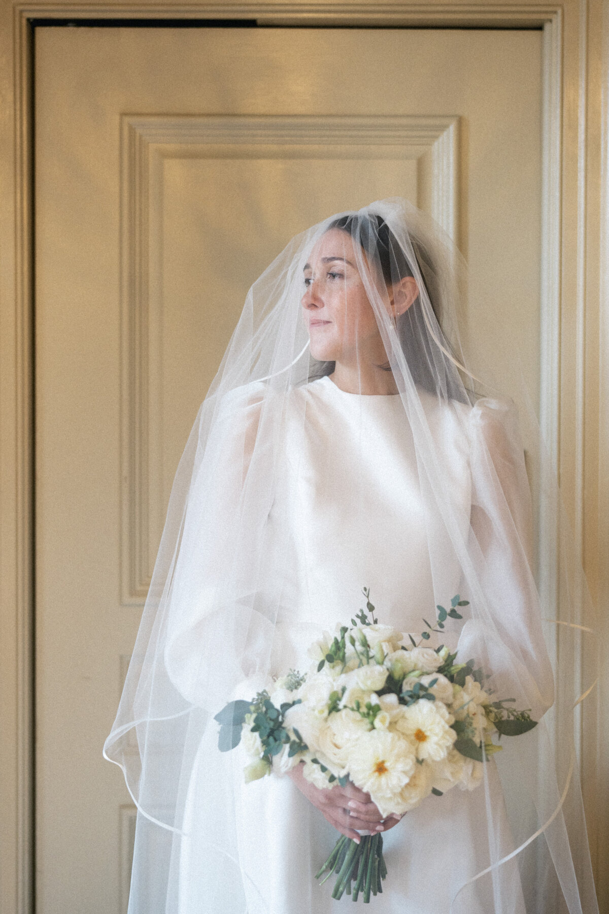 Bride in long-sleeve gown and veil holding white bouquet at intimate Cleveland wedding