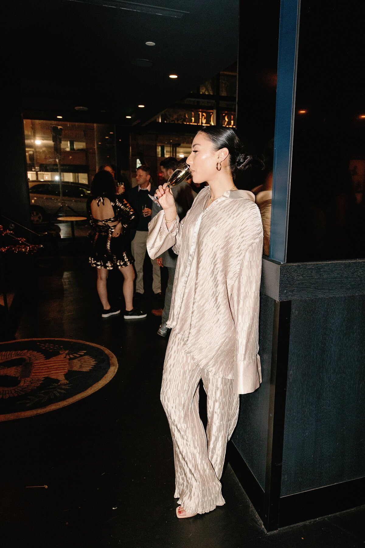 A woman drinks champagne with chic bun and gold shimmering pant suit