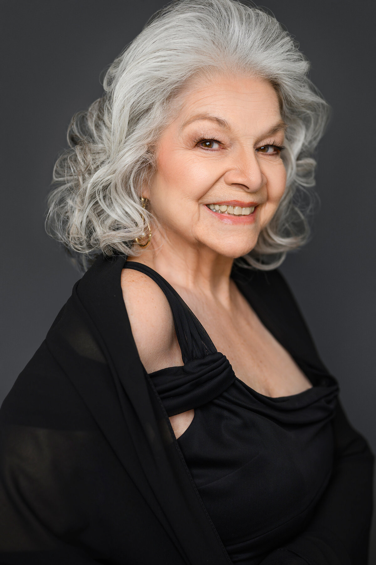Elegant and confident portrait of a senior woman with silver curls, wearing a black dress and shawl