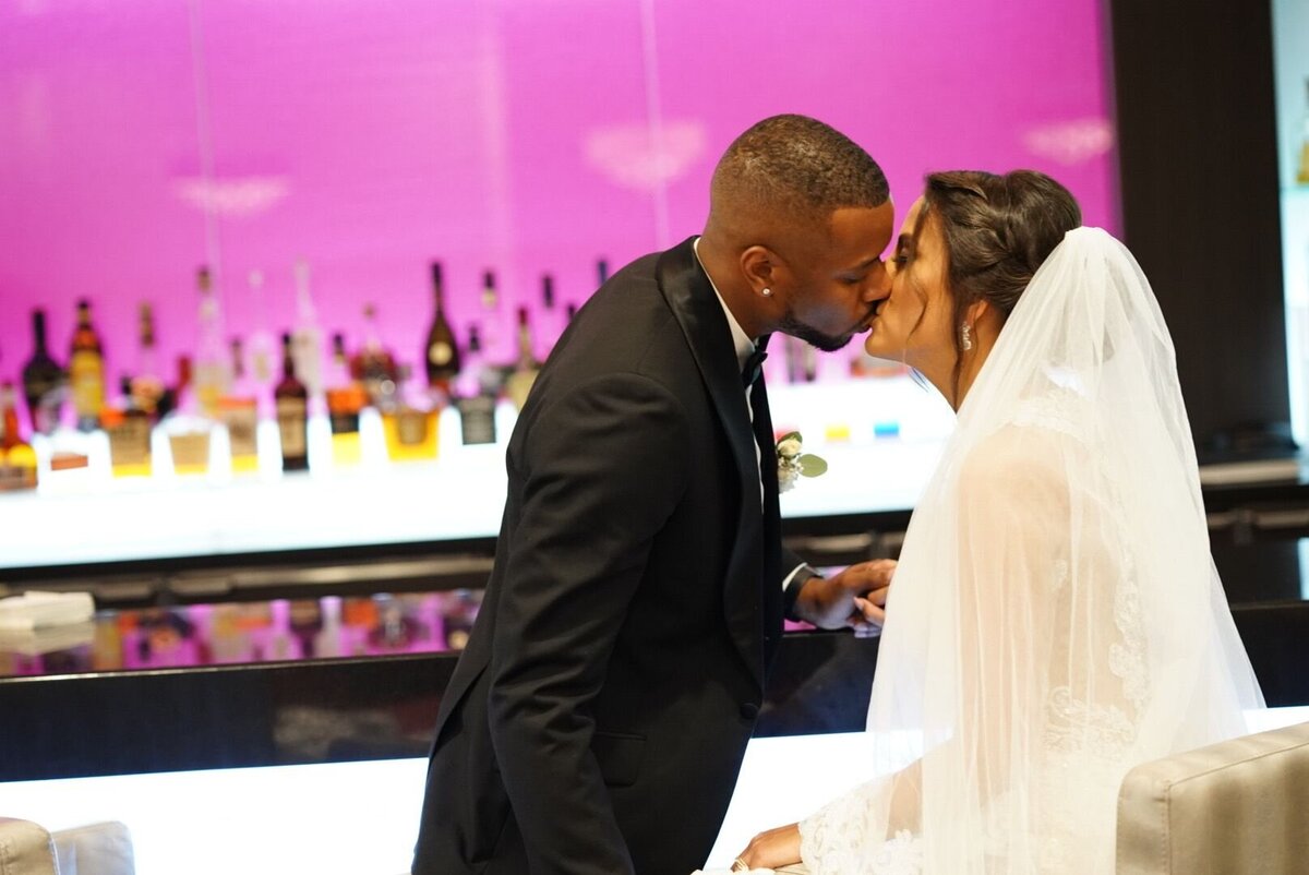 A couple shares a romantic kiss by the bar, surrounded by an elegant and modern setting. The image captures the couple's affection and connection, with the bar's ambiance adding a touch of sophistication to their intimate moment.