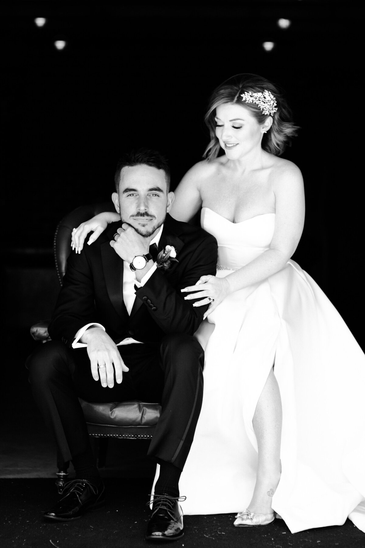 Wedding couple black and white portrait with the groom sitting and bride standing next to him