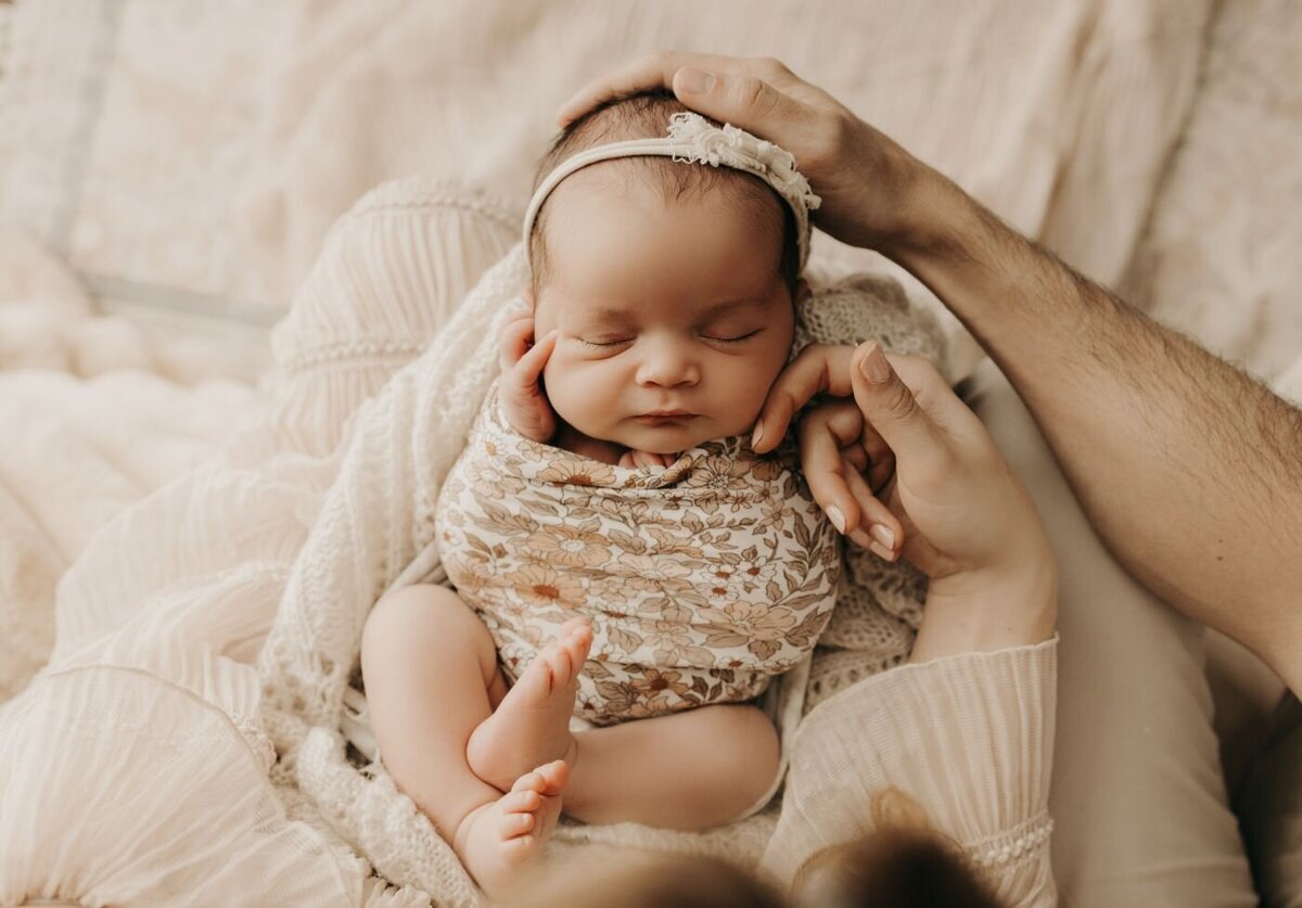 Top-down view of a sleeping newborn baby swaddled in a floral wrap, gently held by parent's hands during a Mullingar photoshoot