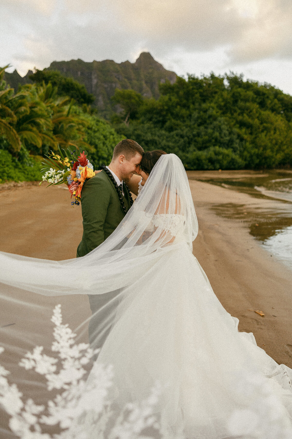 A wedding couple about to kiss as they stand on a sandy beach.