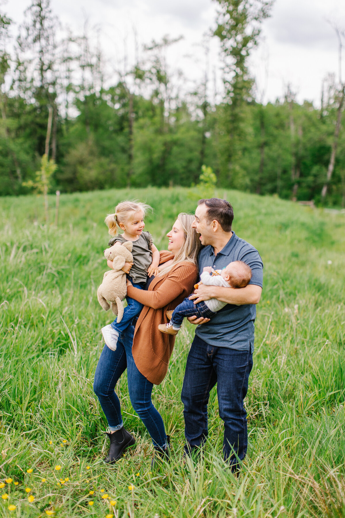 Family of four standing together smiling in a grassy field