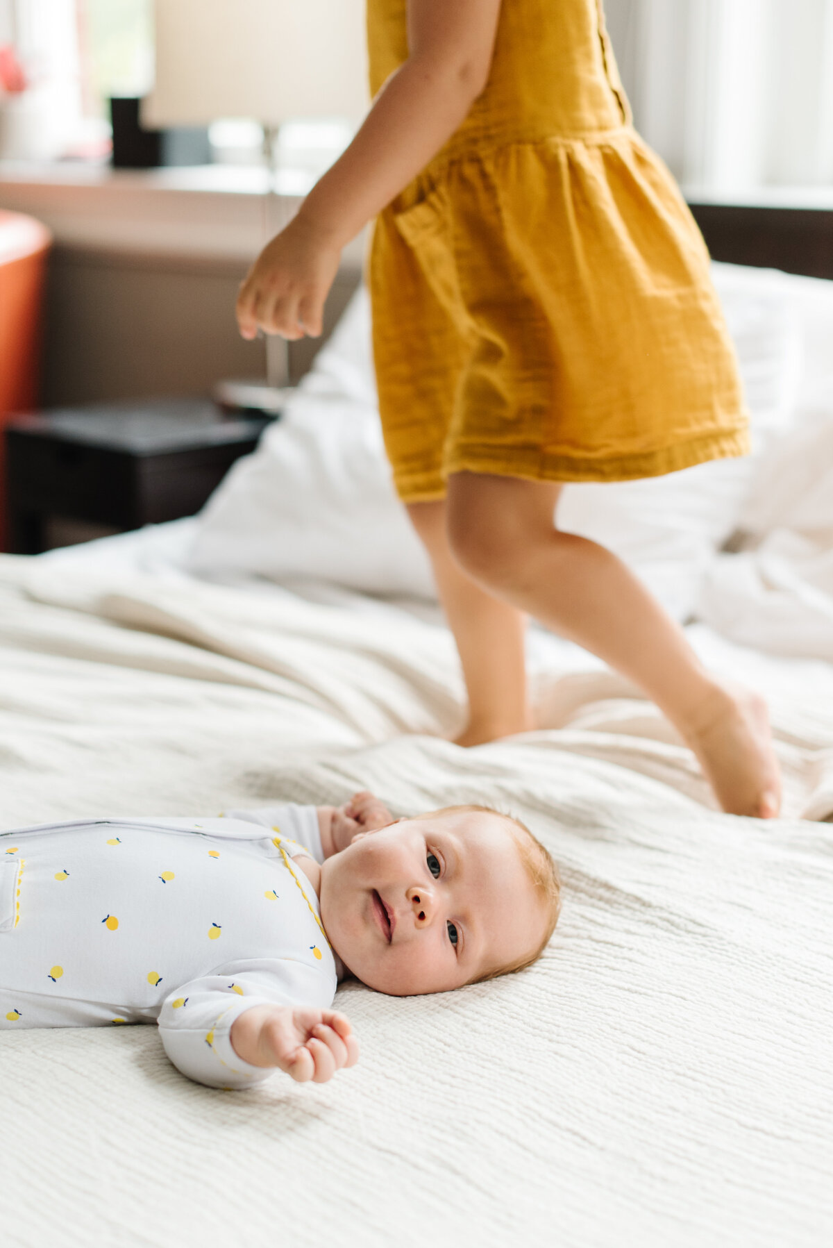 Infant laying on bed with toddler standing on bed behind - Washington DC Newborn Photographer