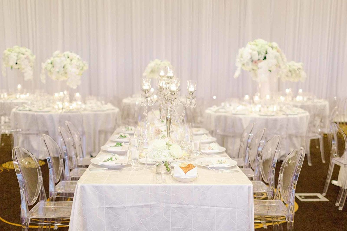 wedding reception with a mixed floorplan of round and rectangular tables, wall draping, clear chairs