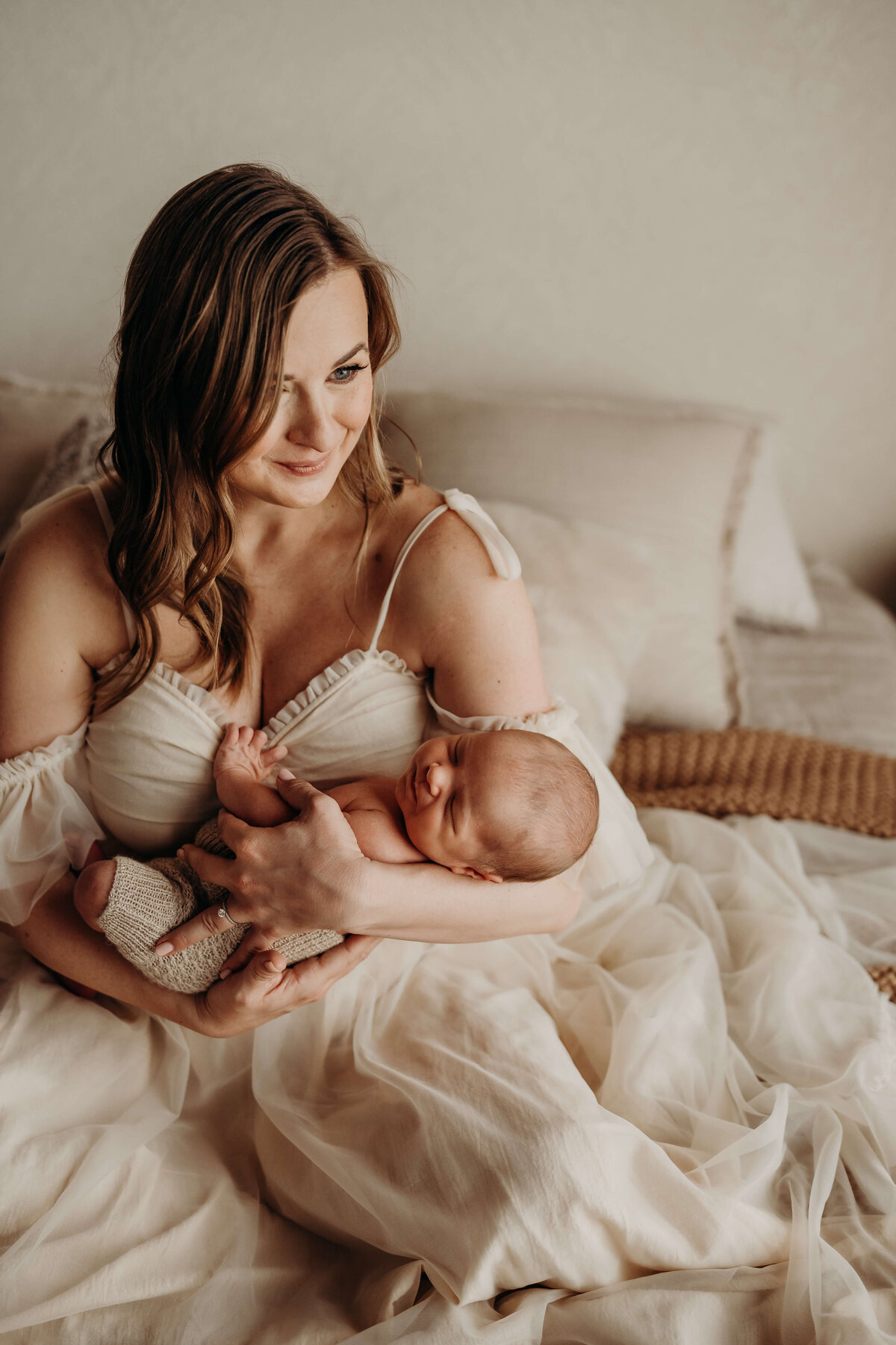 mom smiles as she holds her newborn on a bed