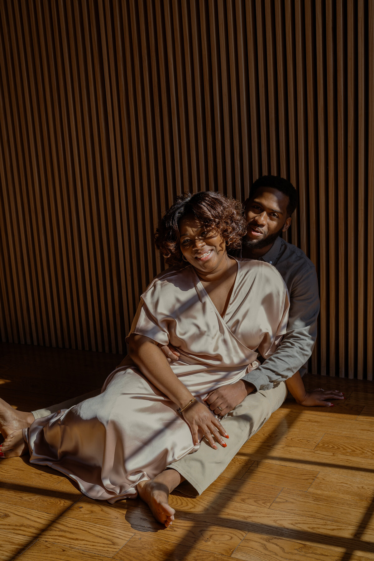 A sophisticated portrait of a mom and dad sitting together in warm, golden sunlight, with bold shadows creating depth and intimacy during an NYC family session.