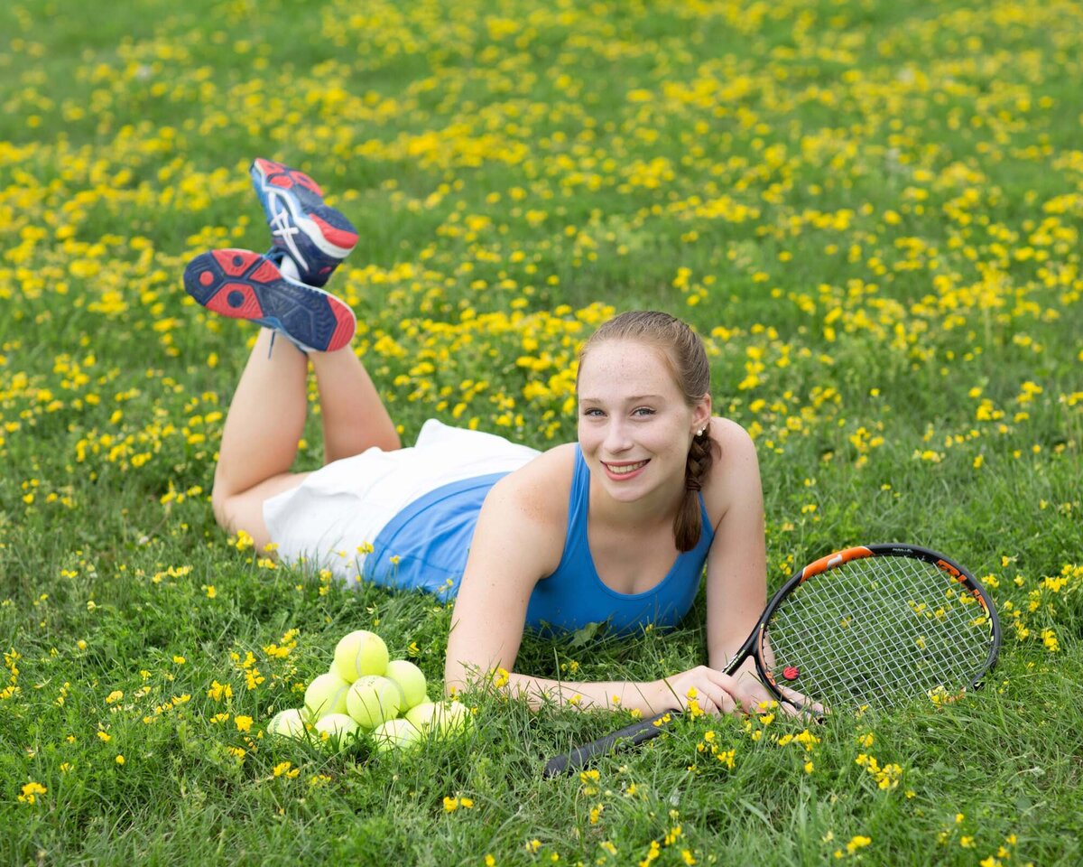 high-school-senior-girl-laying-in-grass-with-tennis-racket