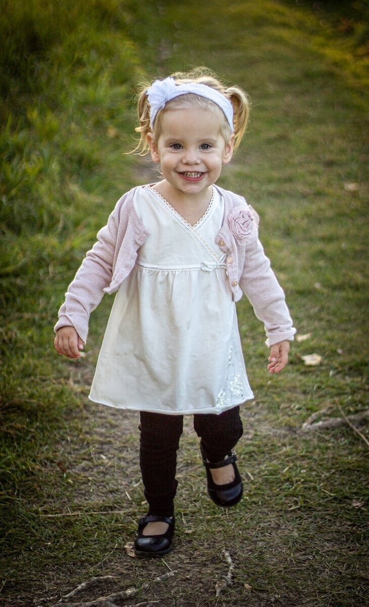 a little girl in a white dress and leggings runs down a dirt road
