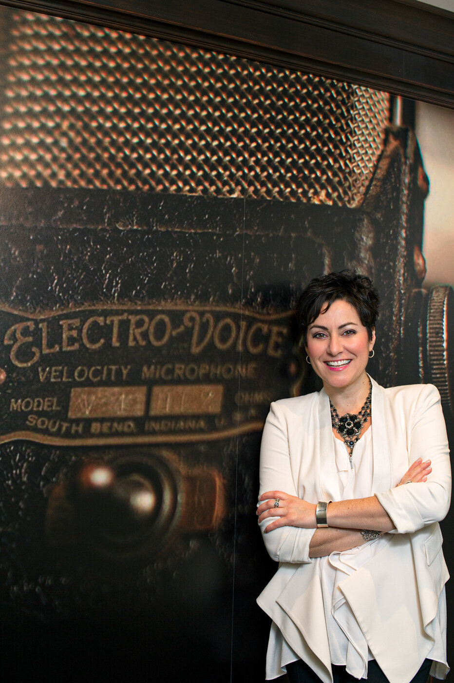 Creative headshot of speaker Tracy Trottenberg posing my a wall size poster of an Electro-voice Velocity microphone.