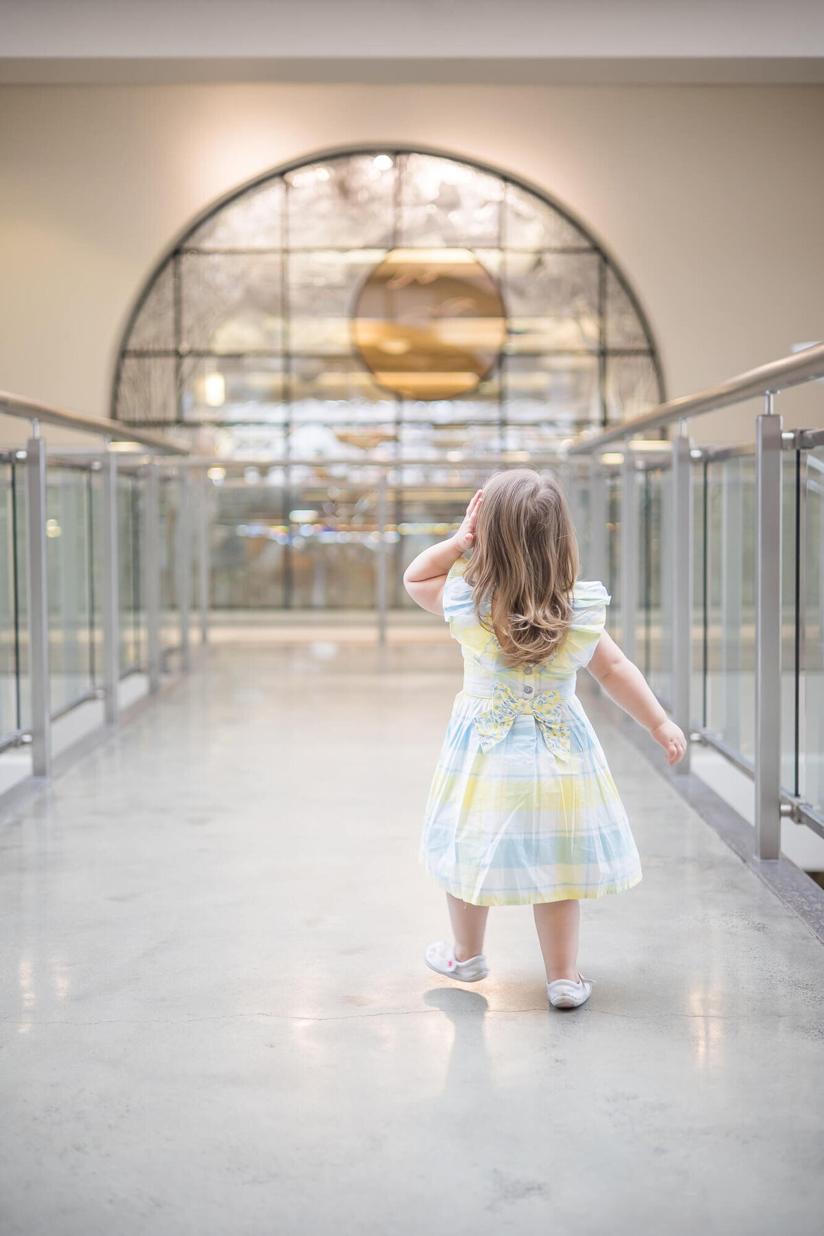 toddler girl in a spring dress on an indoor bridge looking at a stained galss window