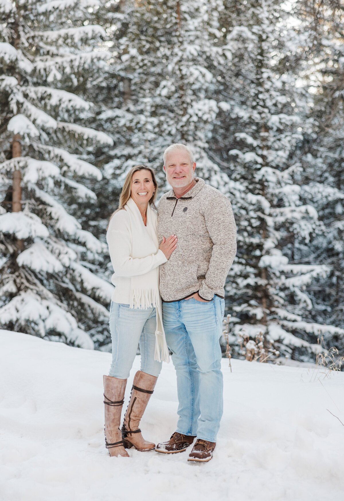 Happy mom and dad smile while hugging in a snowy forest