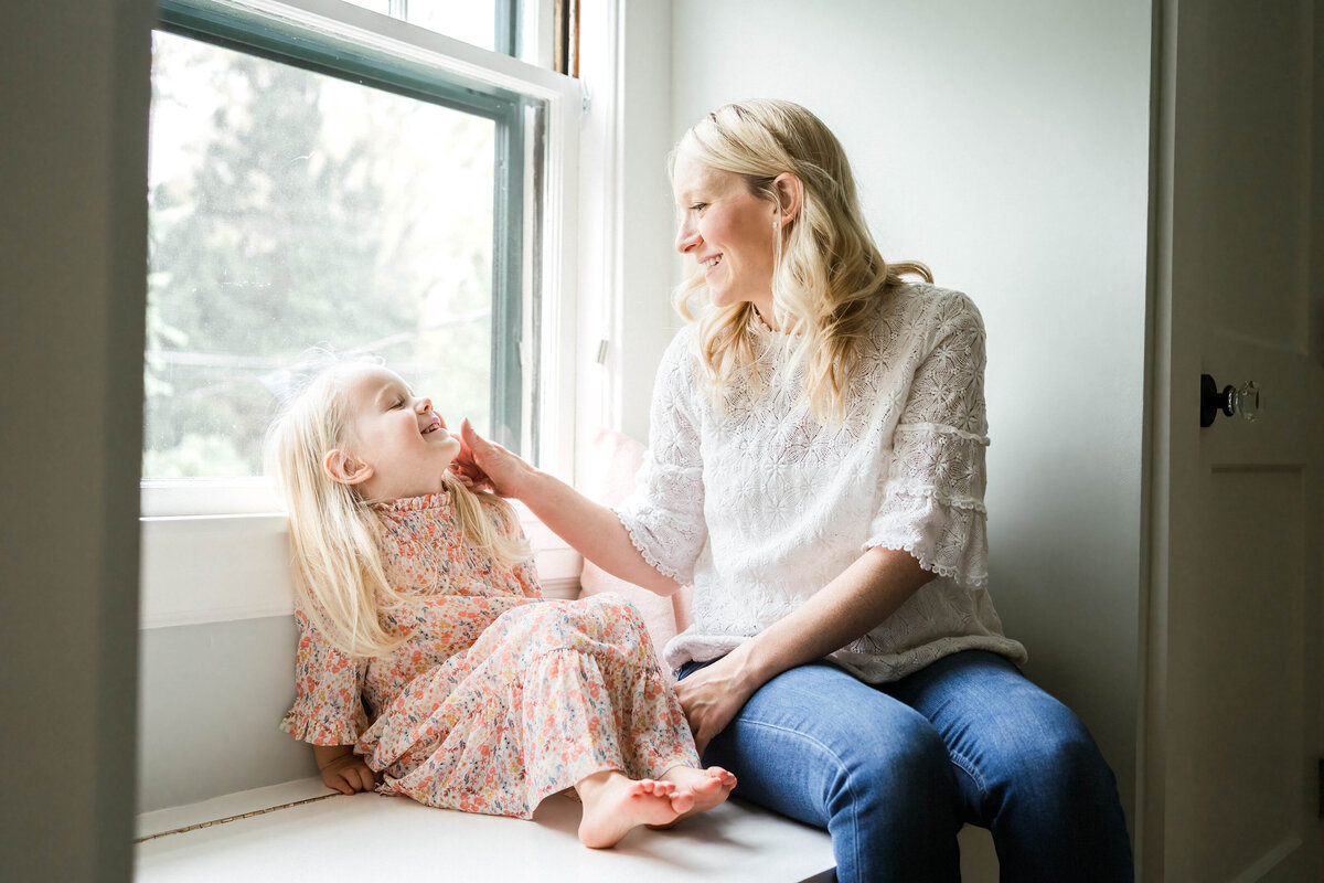 Mom with toddler daughter in window seat with lots of natural light coming in